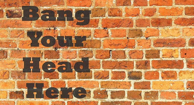 Text on a brick wall reading "Bang Your Head Here".
